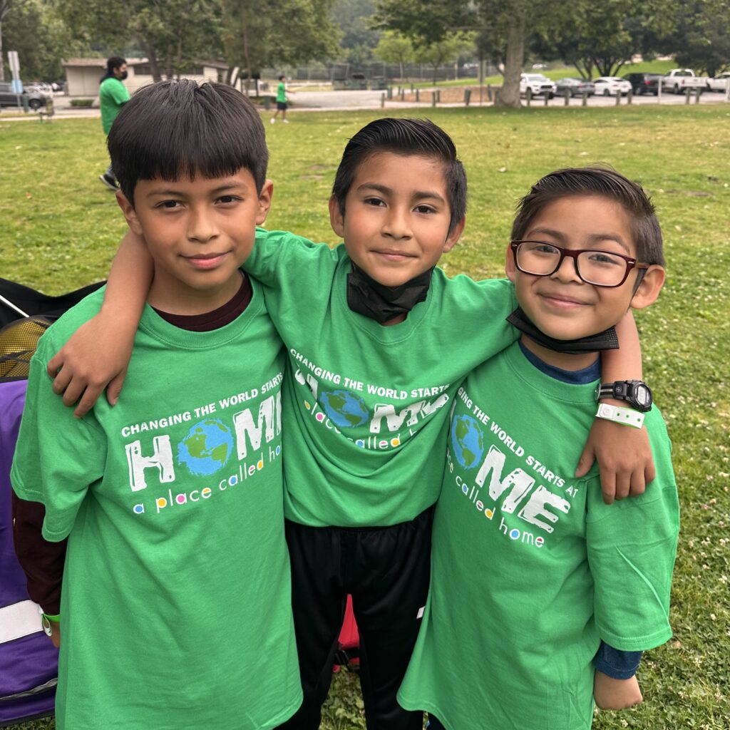 Three young boys smiling together outside in green shirts